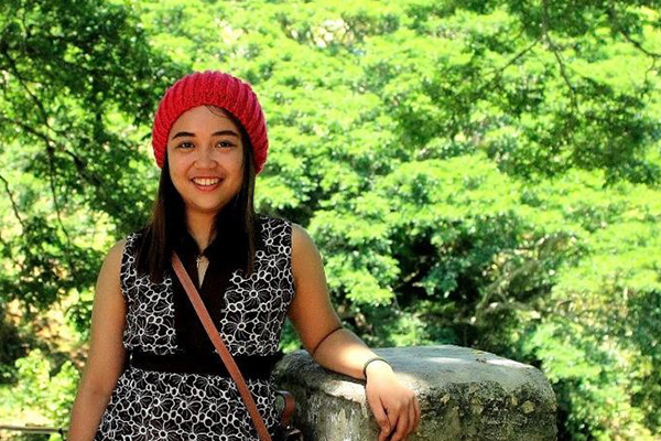Adrienne Mae Perez wearing red beanie standing in front of trees.