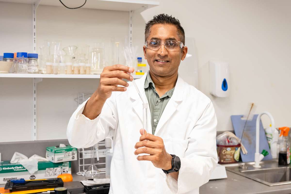 Dr Shaneel Chandra wears a white lab coat and stands in a laboratory.