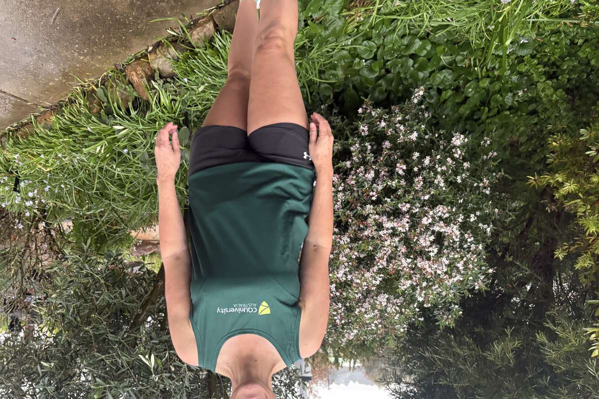 Prof Rachel Bacon wears a green CQU running singlet and stands outdoors smiling.