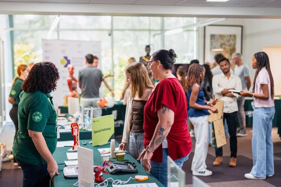 Numerous prospective students walking through a CQU library talking with stalls at an on campus Open Day event