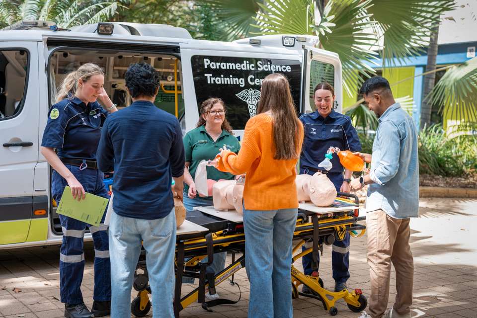 Three prospective students chatting with a paramedicine lecturer and two current students in front of a training ambulance