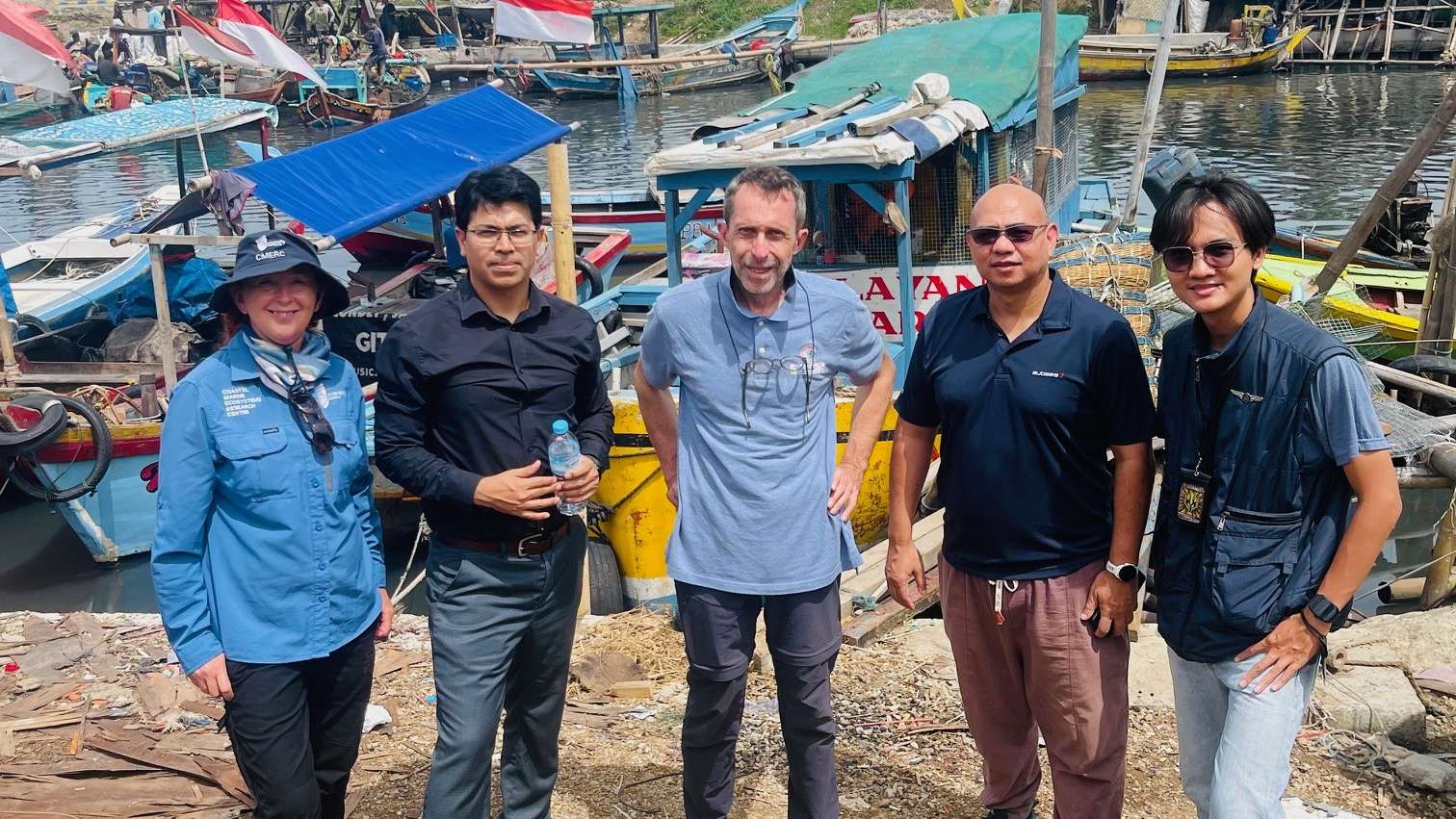 Five people stand on a dock in front of boats in Jakarta.