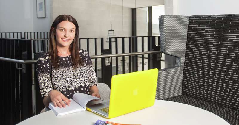 CQU student studying on campus with yellow laptop and smiling